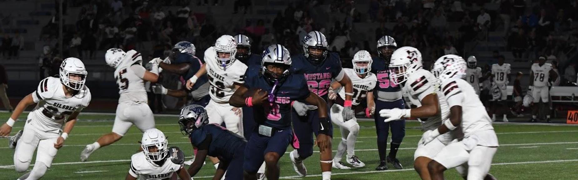 A football player in a pink jersey maneuvers through a crowded field during a game.