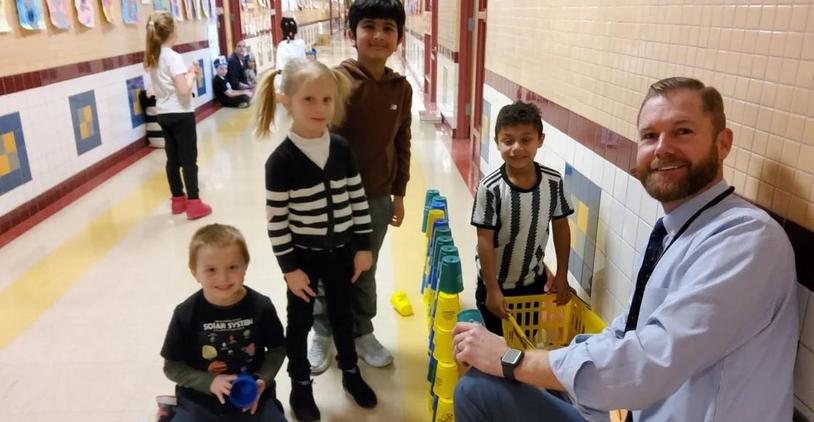 Teacher with students playing with cup stacking in a school hallway.