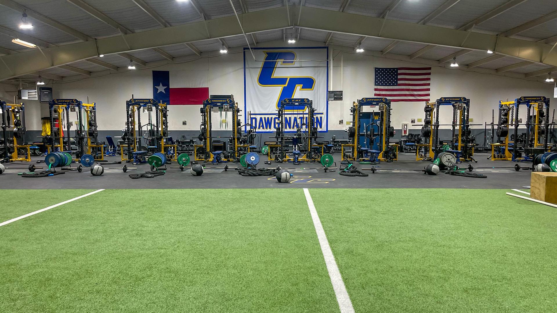 A wide gym with weightlifting equipment and flags hanging on the walls.