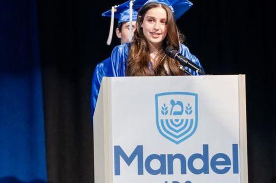A graduate giving a speech at a podium with the 'Mandel' logo in the foreground.