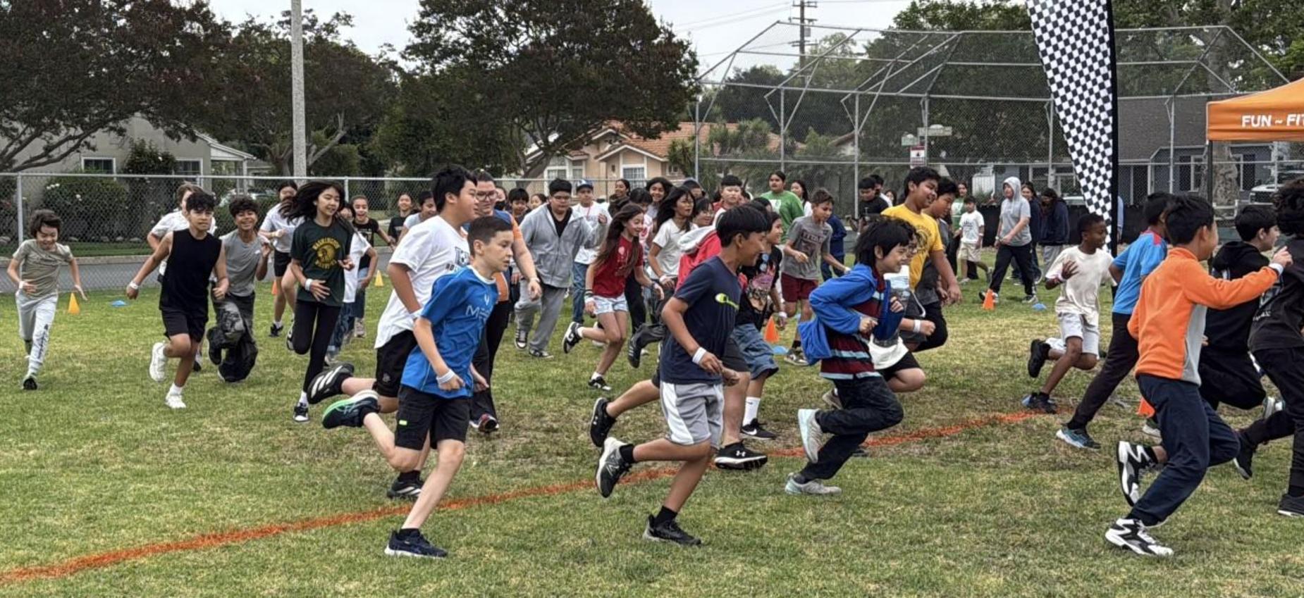 A group of children running energetically on a grassy field during an outdoor event.
