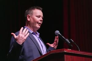 A teacher presenting at Oscar Night, with his hands held out at his sides