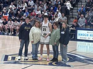 basketball player standing on court holding award with Jim's family around him
