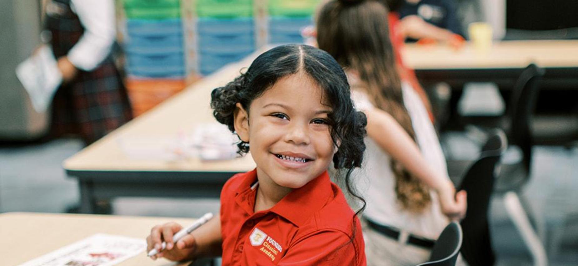 Smiling student in a red polo seated at her desk in the classroom