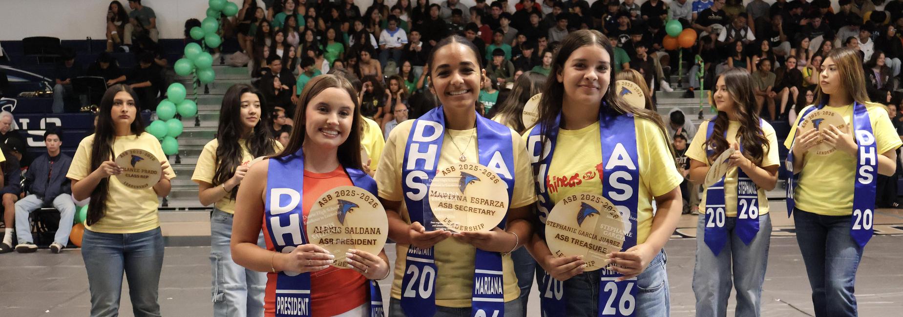 Three smiling students holding awards during a school event.