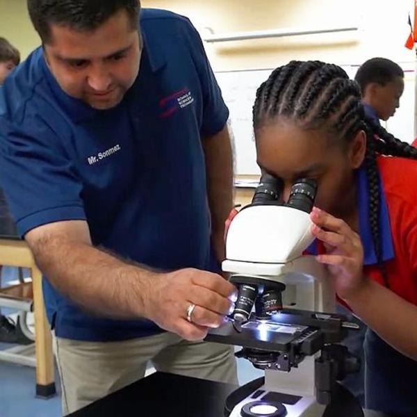 Teacher assisting student looking through microscope.