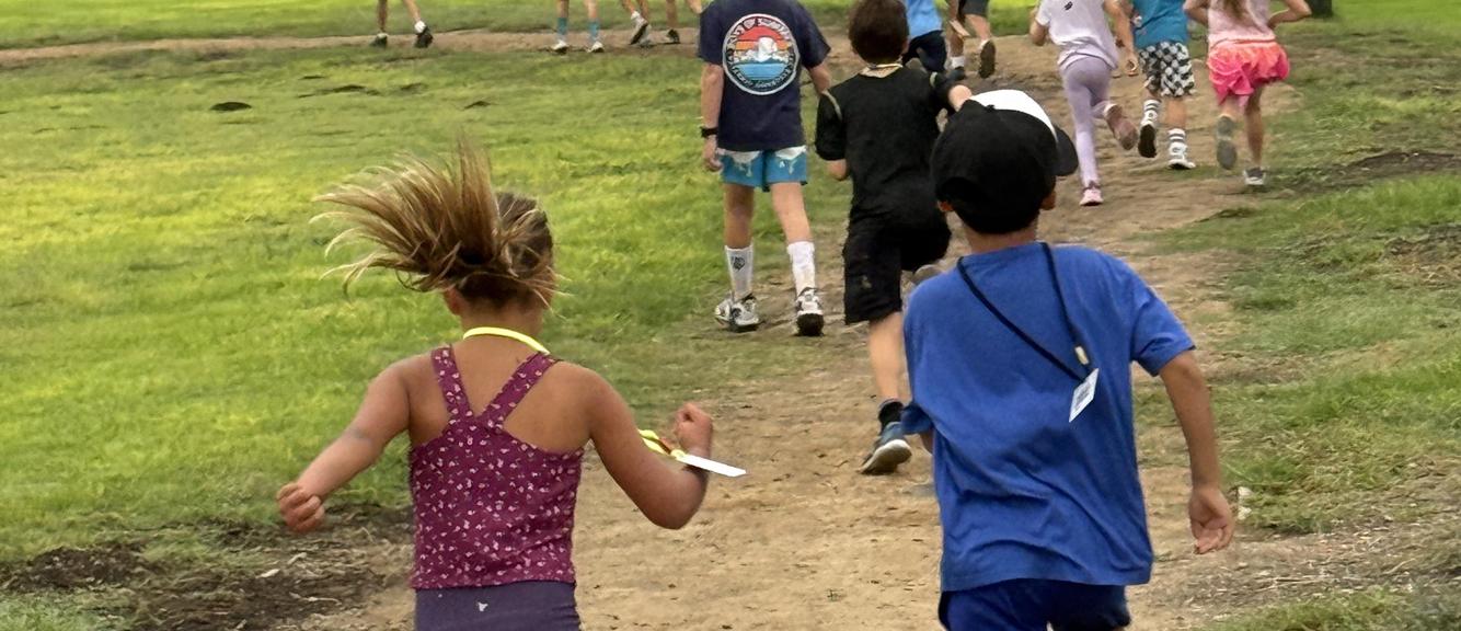 Children running on a path in a grassy area during an outdoor activity.