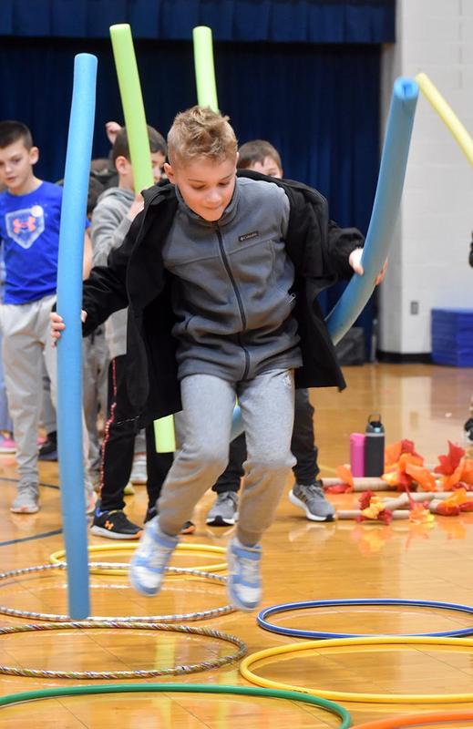 a student holding pool noodles and jumping over hula hoops