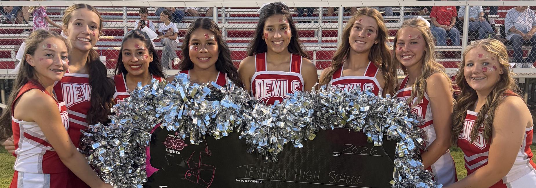 Cheerleaders hold a large check for $5,000 at a school event.