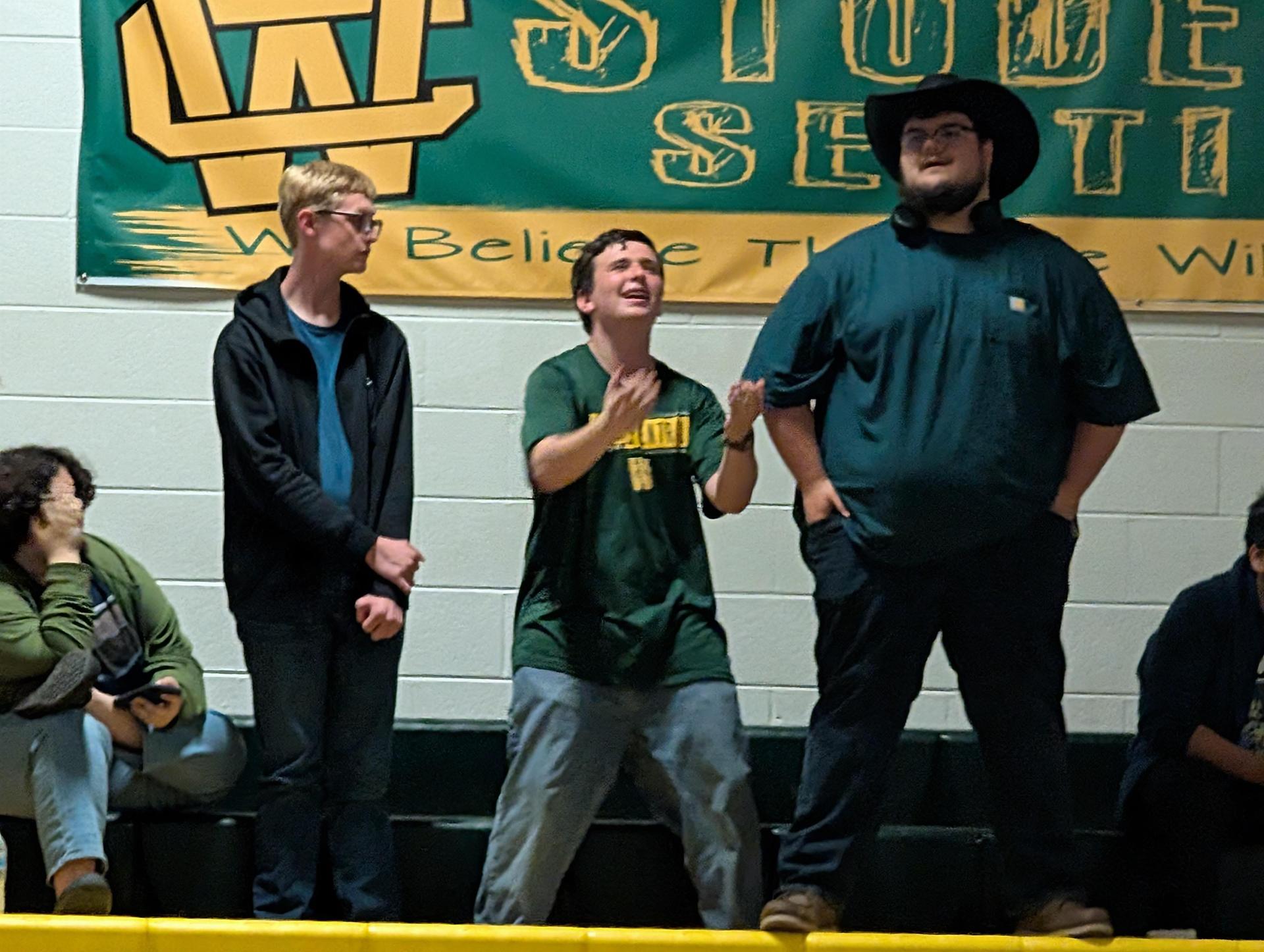 Three students in casual attire engaging with the crowd in a school setting.