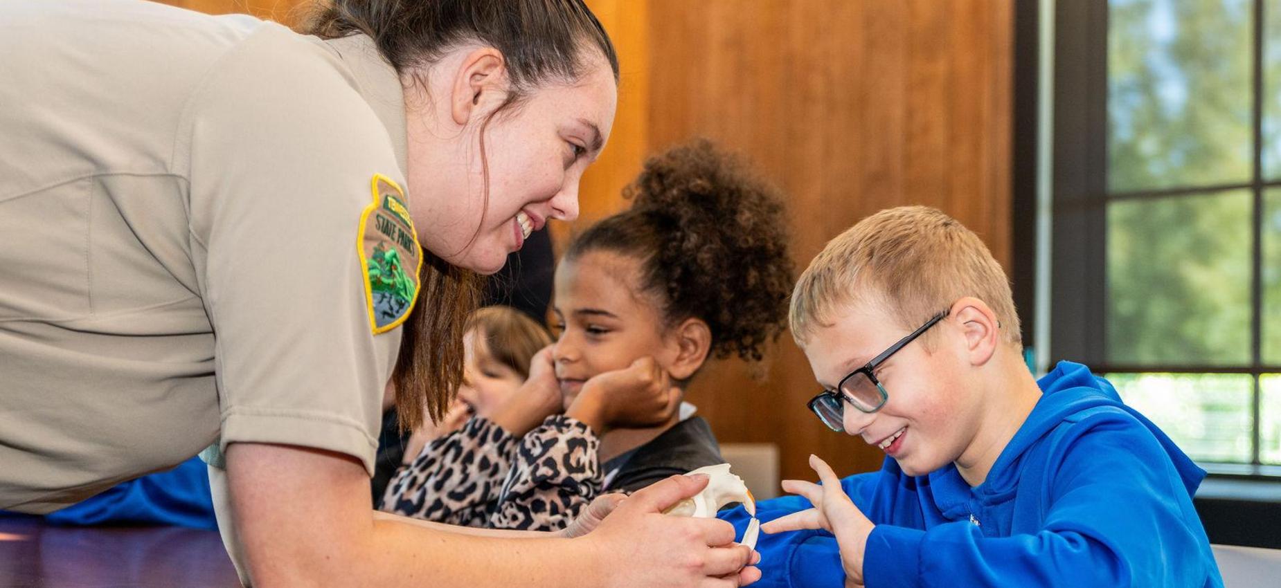 A park ranger interacts with a child at a table while others look on.