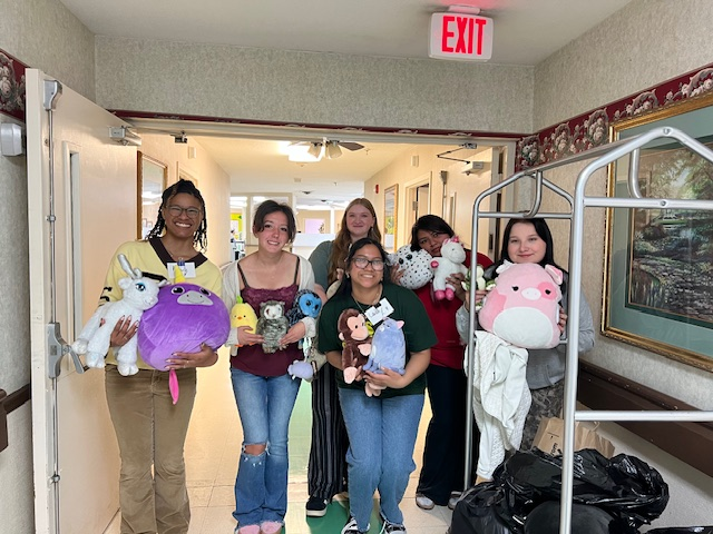 Group of six girls holding plush toys in a hallway.