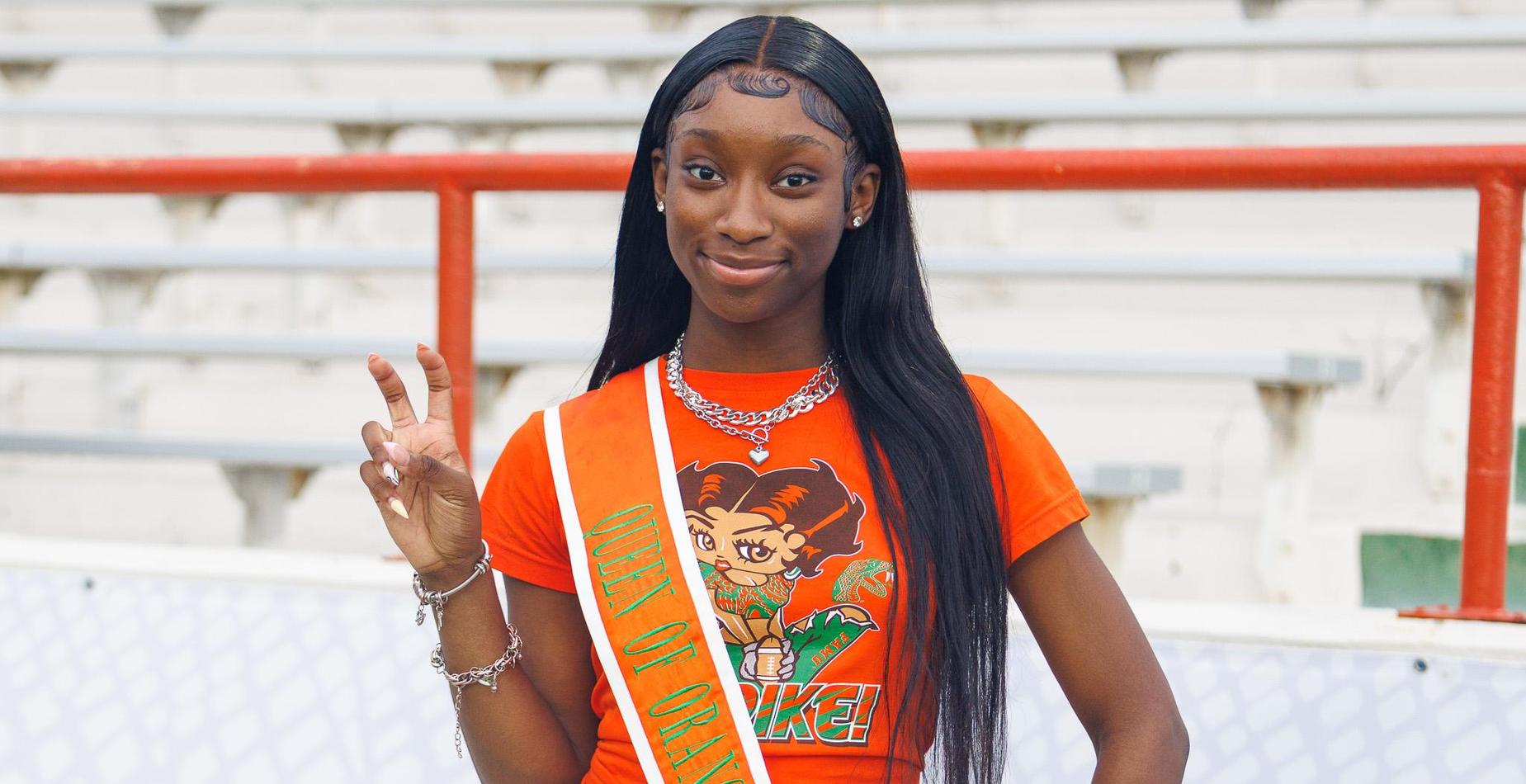Young woman in orange shirt and sash, smiling with peace sign.