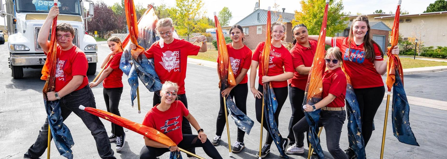 Group of performers in red shirts holding flags with colorful patterns outdoors.