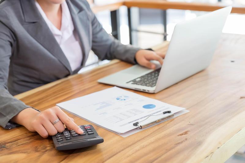 Young business woman working on laptop with a calculator