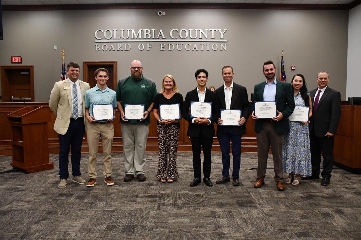 8 adults lined up. Some are holding awards.