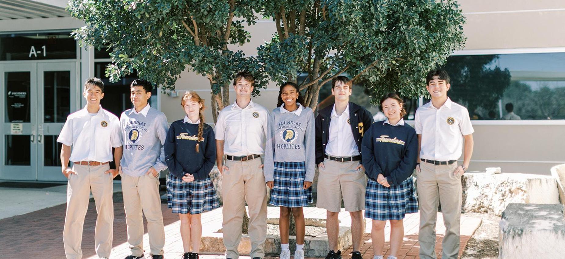 Group of students in uniform, from the youngest grades through high school, stands together outside the school