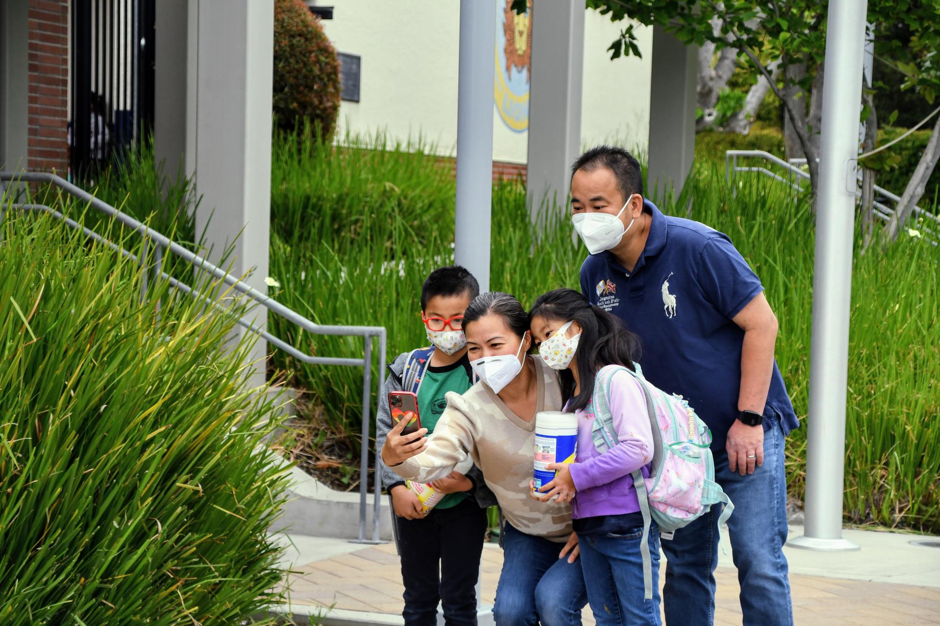 Family in masks smile for a selfie