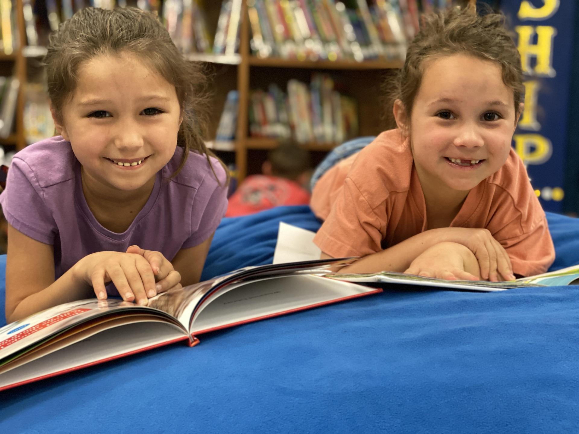 2 smiling girls reading a book