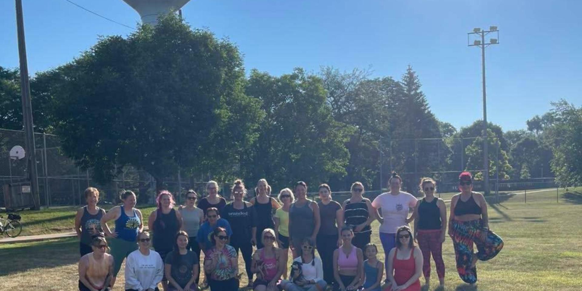 A large group of people posing outdoors in a park on a sunny day.