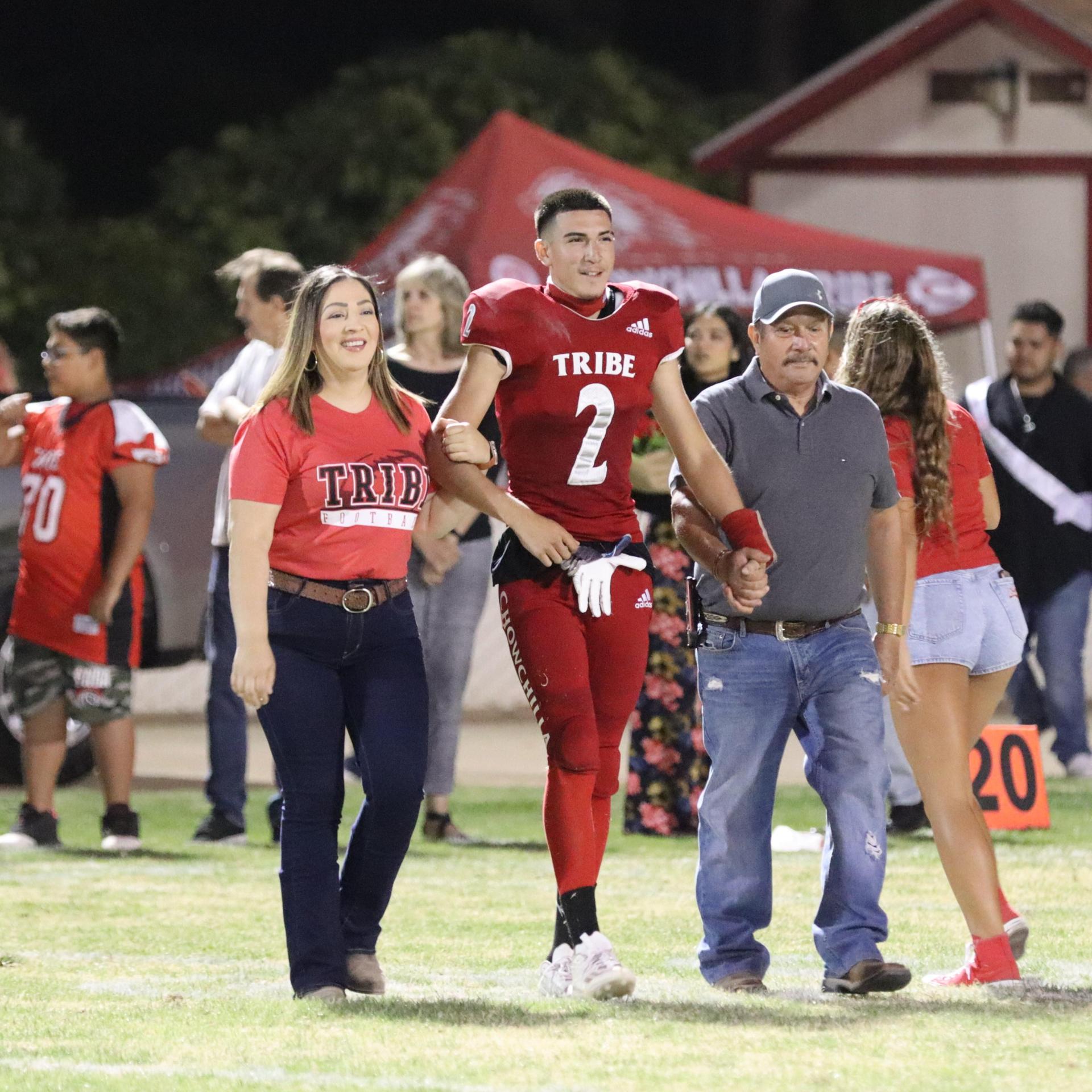 homecoming king and queen candidates walking across the field with their escortshomecoming king and queen candidates walking across the field with their escorts