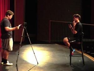A student interviews and films a player in the auditoirum.