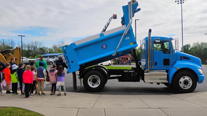 Students gather next to a raised blue dump truck during the 