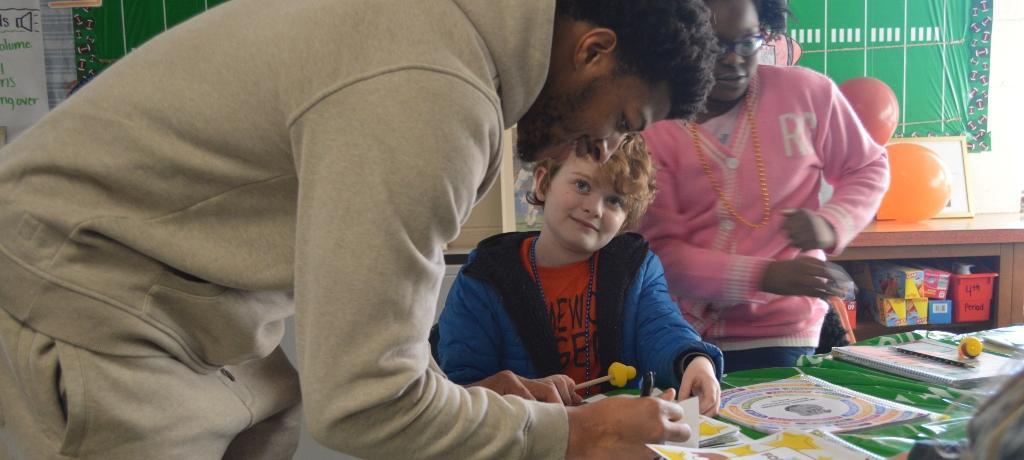 Boy looks on with adoring gaze as football player autographs  paper
