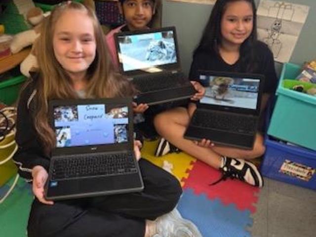 Three girls sit on the floor, each holding a laptop displaying their work.