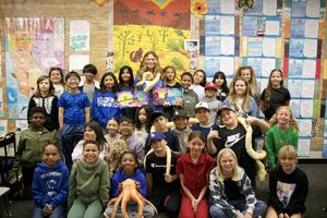 Teacher Lindsay Hill holds four books while standing with her students.