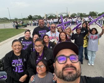 Group of people in matching shirts at an outdoor event with purple cheer sticks.
