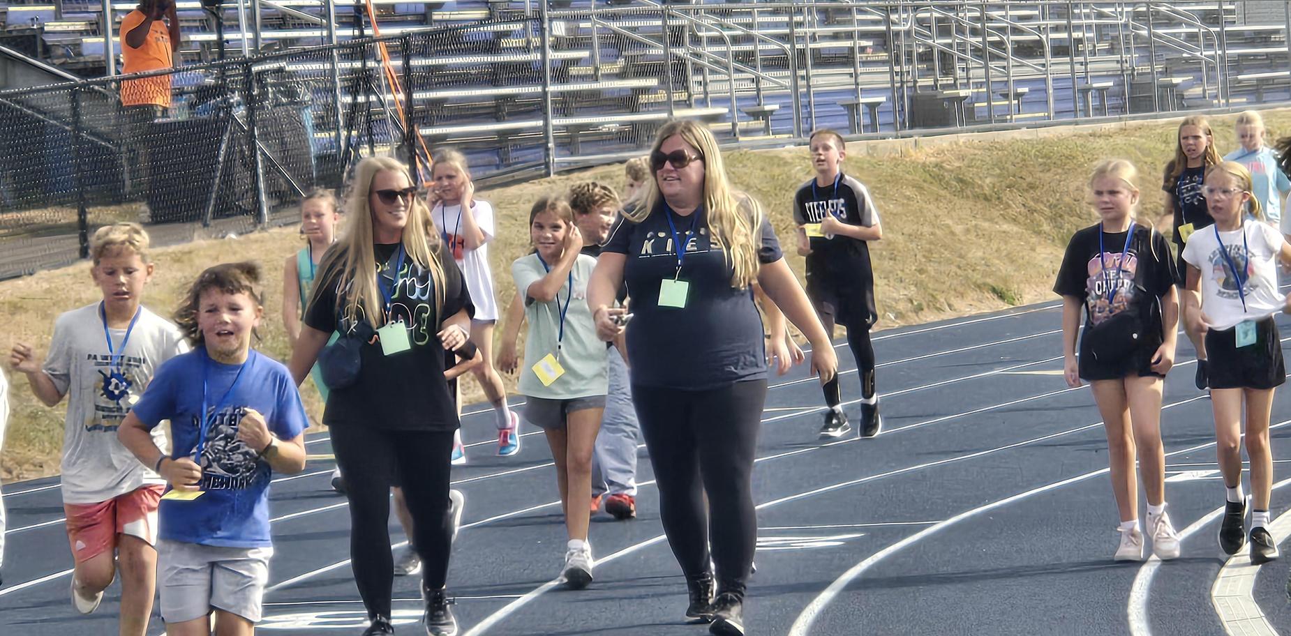 Kids and adults interacting while walking on a track during a school event.