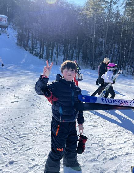 Boy in ski jacket gives a peace sign on a snowy slope.
