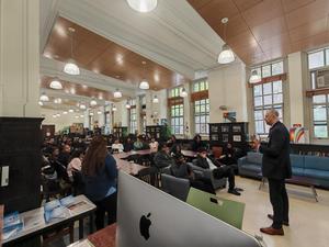 Speaker engaging a large audience in a spacious area with modern furniture.