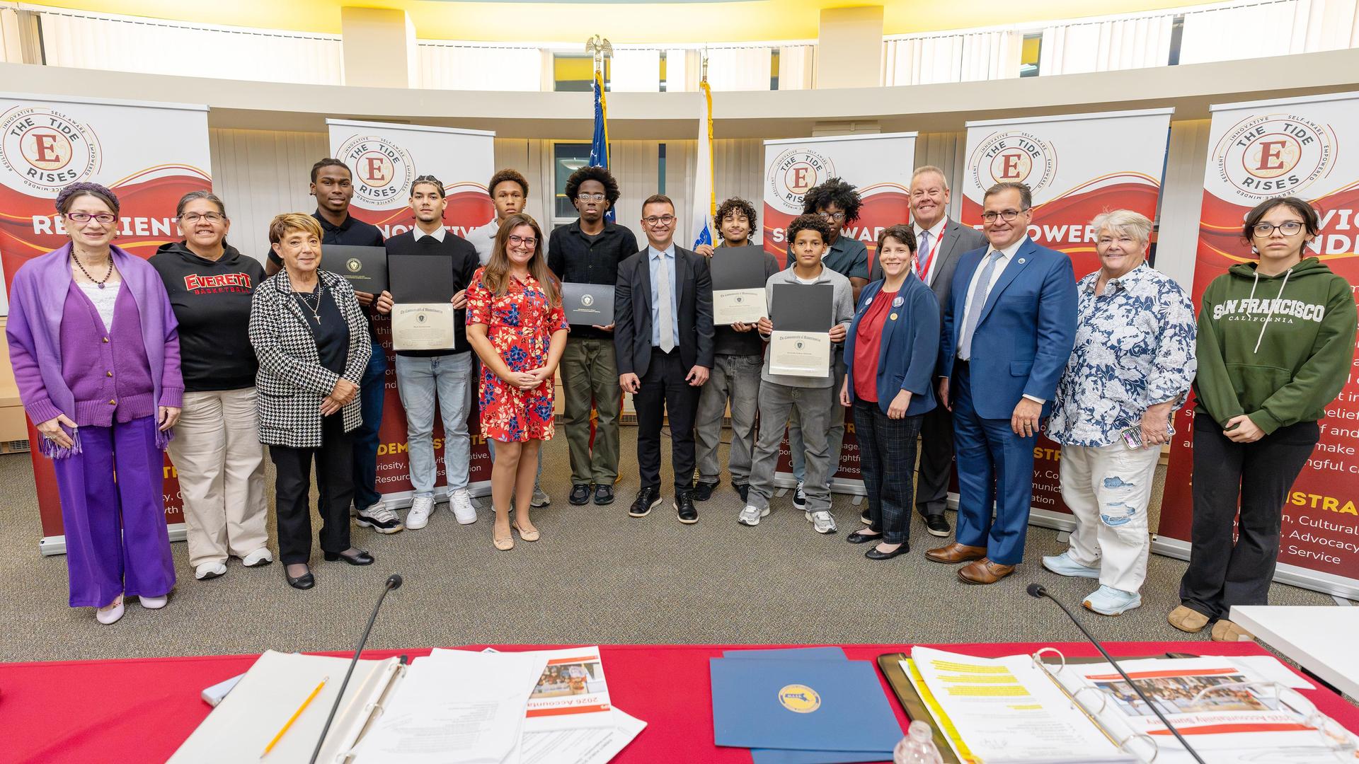 Group of students and adults pose with certificates in a meeting room.