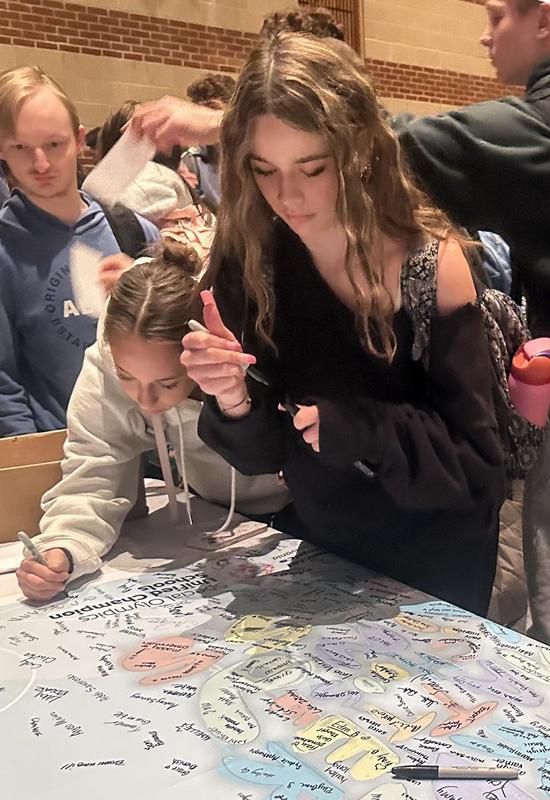 Two girls adding their signatures to a banner on a table