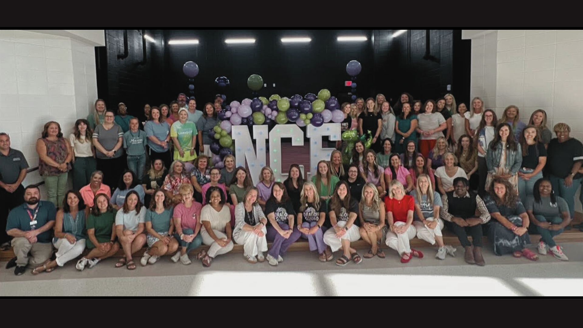 A large group of diverse people posing together in front of a decorated backdrop with balloons.