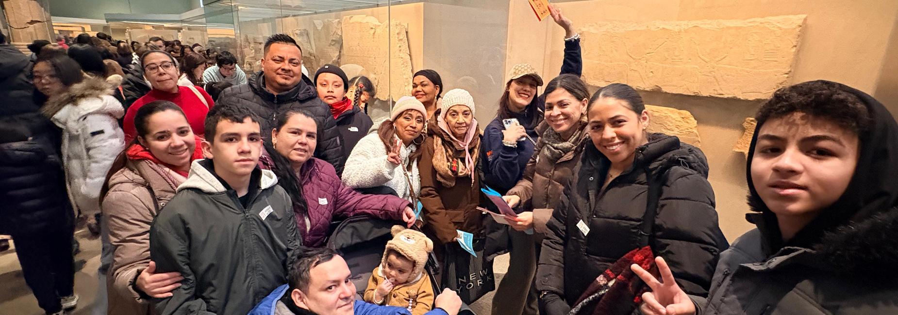 A diverse group of people posing together in a museum with ancient artifacts in the background.