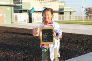 Girl holding a chalkboard sign celebrating the first day of 5th grade