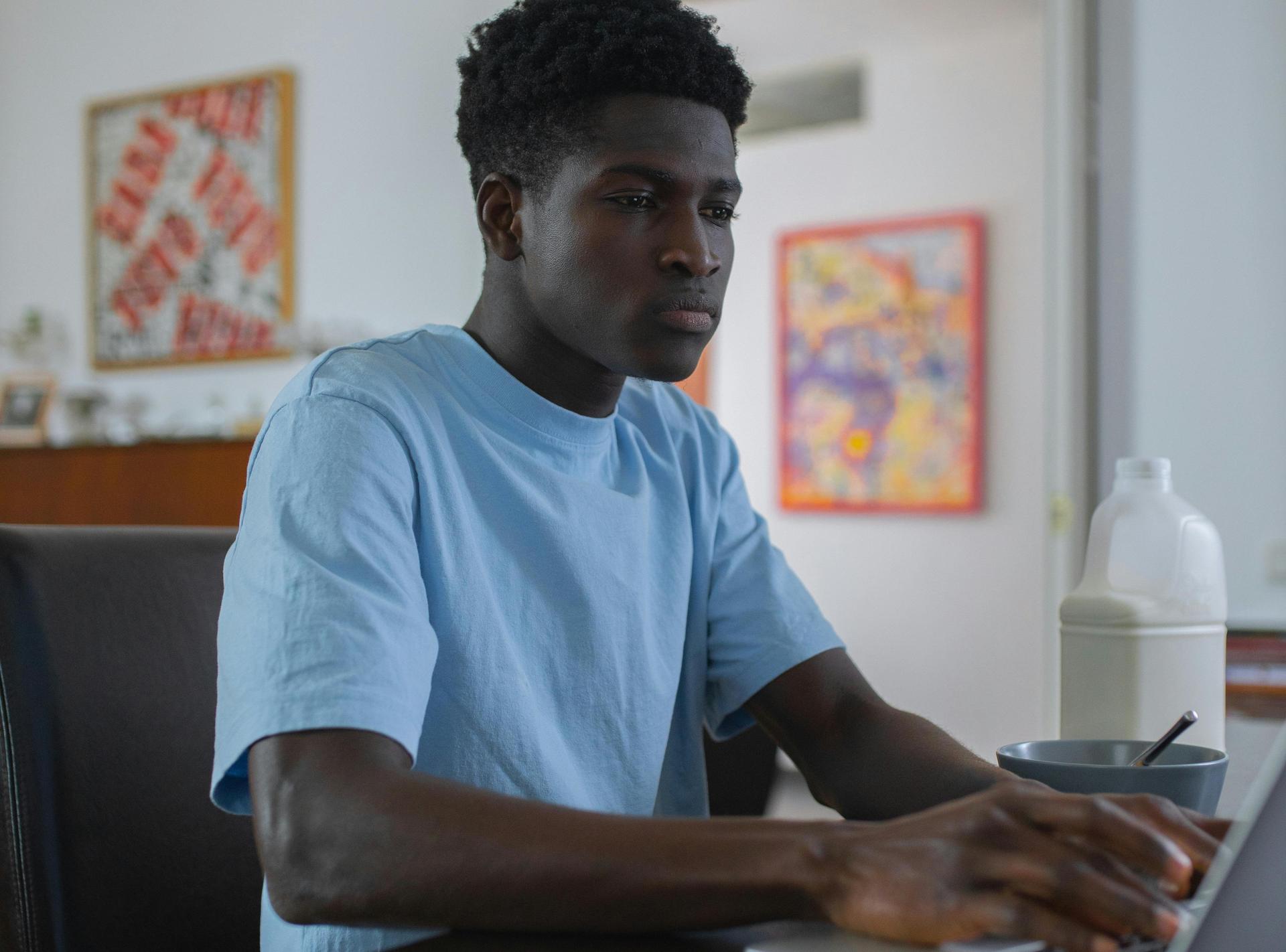 A young man focused on a laptop while seated at a table.
