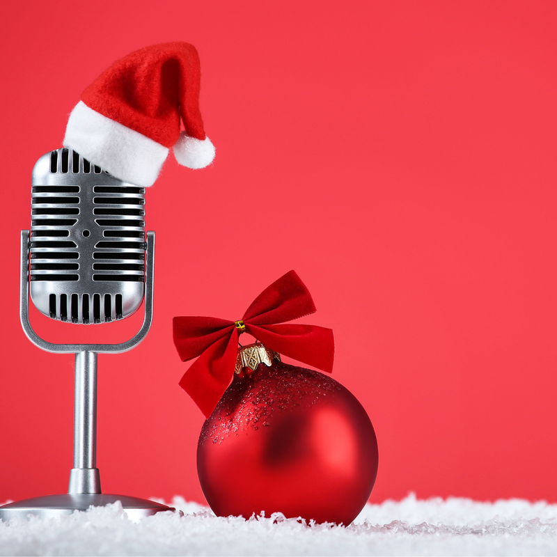 A vintage microphone with a Santa hat beside a red Christmas ornament with a bow.