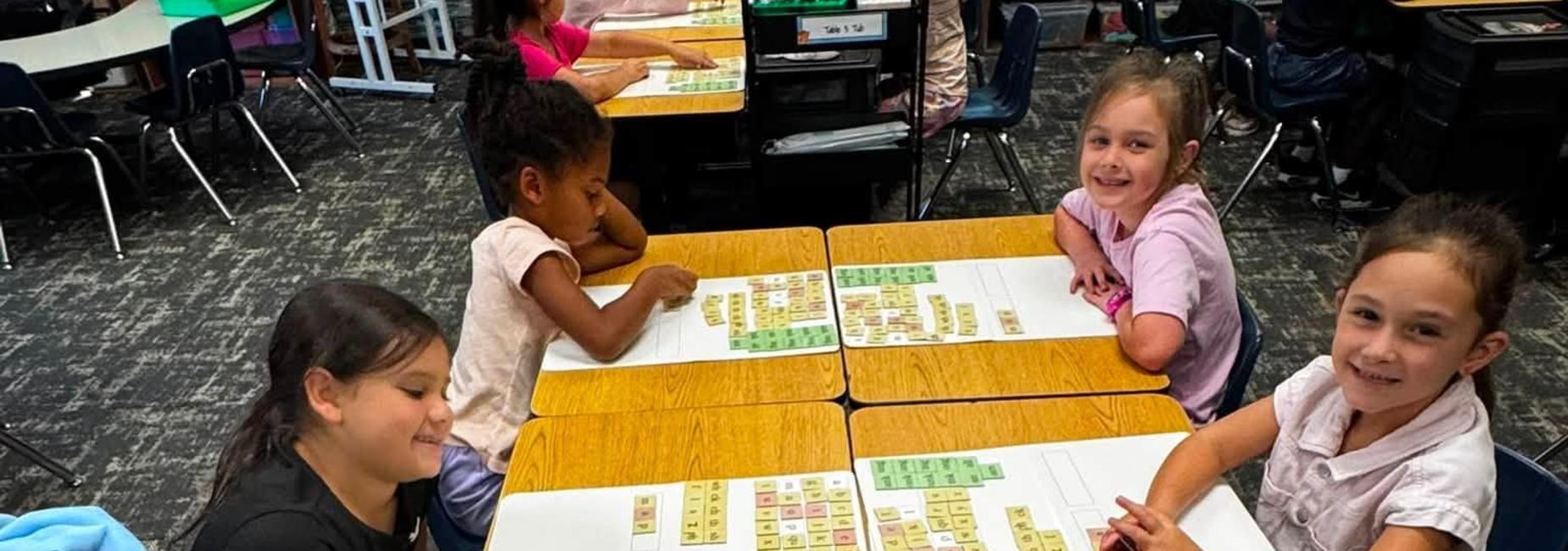 Students engaged in a classroom activity with colored letters on tables.