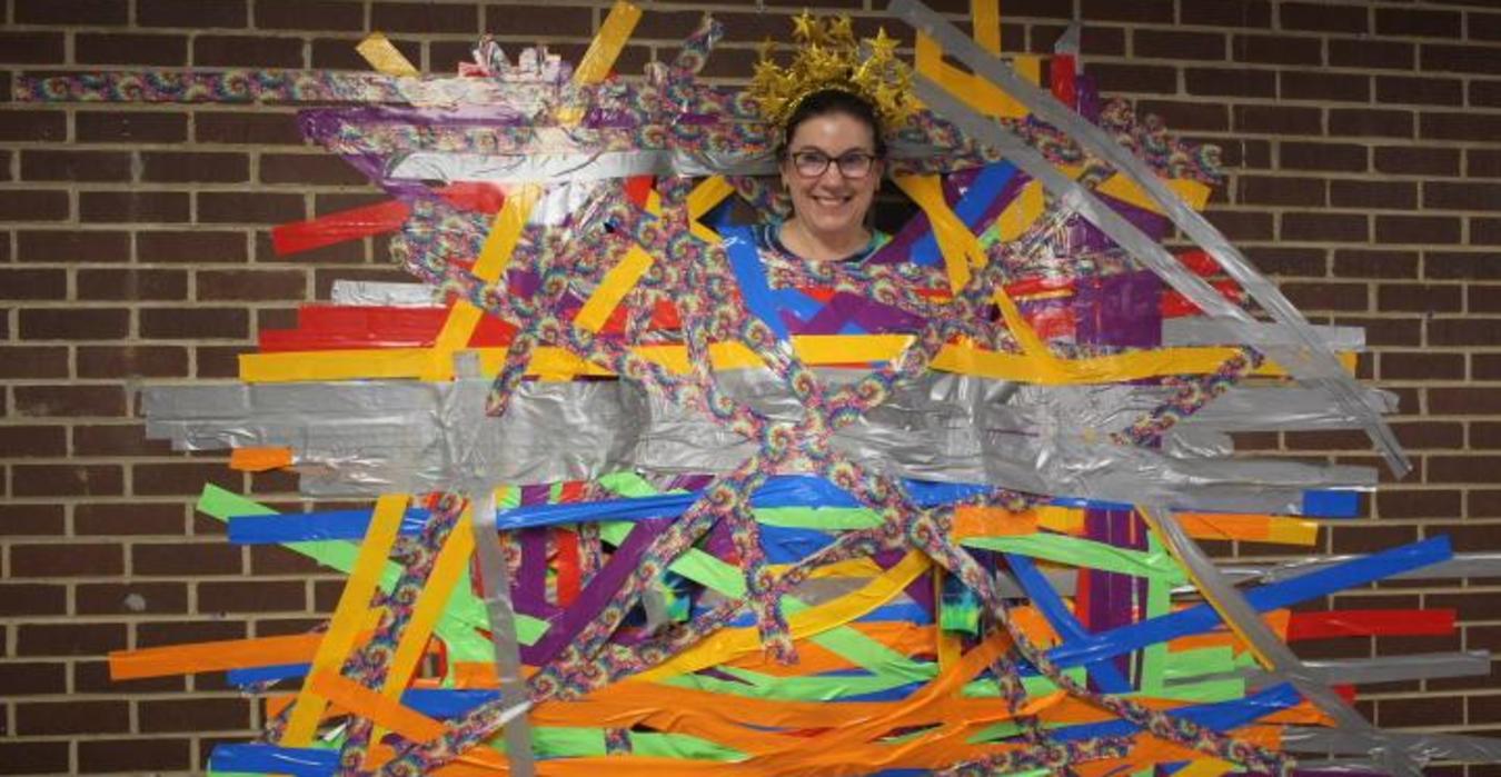 Person standing amidst colorful tape art on a brick wall.