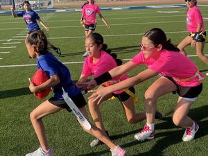 one girl runs with ball and two others try and take her flag
