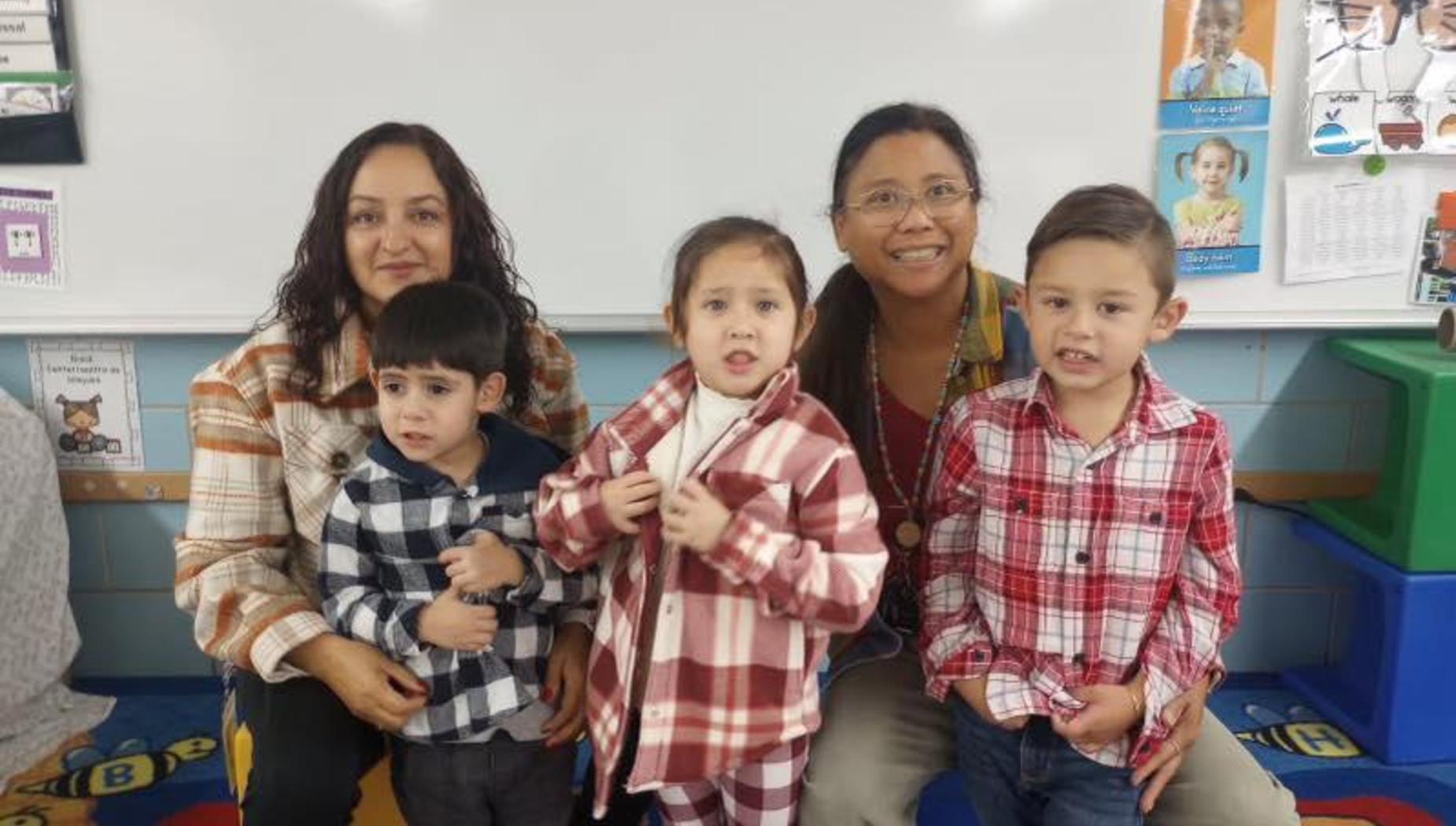 Two adults and two children wearing matching flannel shirts in a classroom setting.