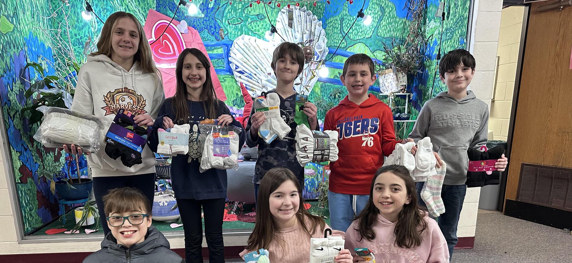 Children holding donated clothing items in a school hallway.