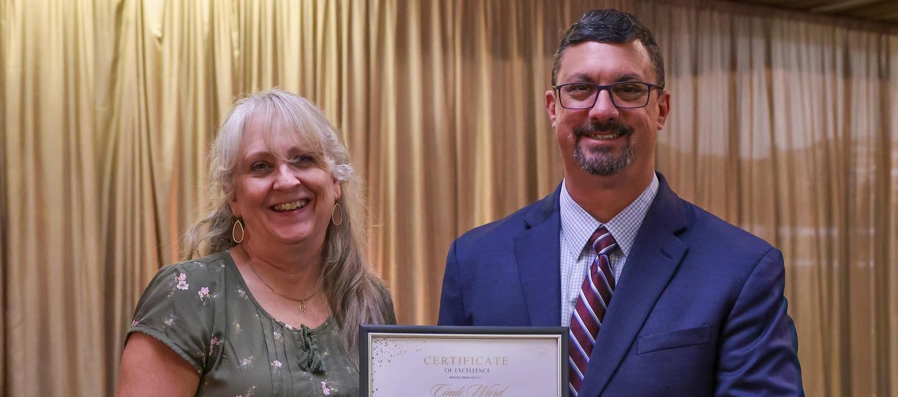 Two smiling people holding a certificate in a formal setting.
