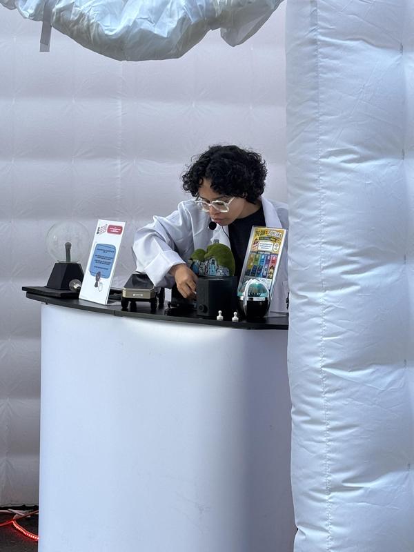 A person in a lab coat demonstrating an experiment at a booth.