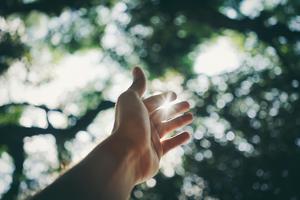 A hand stretched upward, with the sun peeking through two fingers