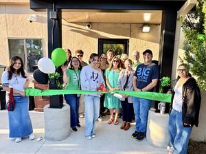 People cut a green ribbon in front of a building